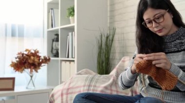 kanepede oturan ve sonbahar mevsiminde kış geliyor ve evde oturma odasında örgü mevsimlik yapma şirin Asyalı kadın