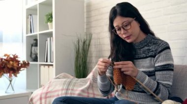 Asyalı kadın dışında pencereden bakarak ve sonbahar mevsiminde kış geliyor ve evde oturma odasında örgü mevsimlik yapma kanepede oturan sevimli