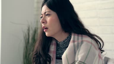 Asyalı kadın soğuk hissediyorum yakalar burun kaşıntı rahatsız ve kışın evde oturma odasında sneeze.