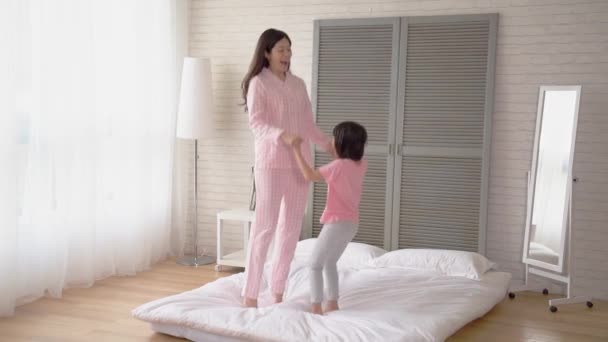 ママと女の子の柔らかいベッドで一緒にジャンプします 彼らは夢中になって笑うし 寝室に大声で叫ぶ — ストック動画