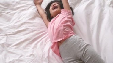 Yatağa haddeleme onun Kol germe sevimli sevimli genç kadın çocuk. Pembe pijama giyiyor. O bu rahat yatak ve hoş güneş ışığı sahiptir. Üzerinde yan yukarıda. Yavaş hareket kavramı.