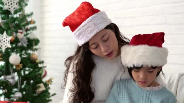 小可爱的亚洲女孩听一个圣诞节故事从她的母亲在家里的客厅读一本书 — 图库视频影像