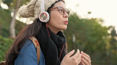casual Asya kız giyiyor eşarp ve sıcak tutmak, güneşli Kent Park müzik zevk için ellerini rub.