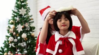 güzel Asya anne evde oturma odasında Santa şapka giymek onun mutlu sevimli küçük Asyalı çocuk yardımcı olur. Kış tatil tatil kavramı.