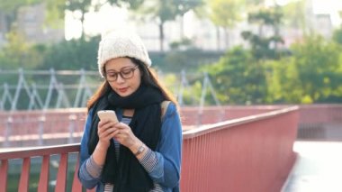 Smartphone manifatura kız Köprüsü'nde kentsel City, telefon okuma veya yün şapkası ile kışın sosyal medya kullanarak tutan Asyalı kadın.