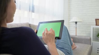 mutlu gülümseyen kadın mobil dijital tablet kullanma ve online video film güneşli tatil sırasında rahatlatıcı izlerken kanepede uzanmış. Yeşil perde kopya alanı ile oynamak.