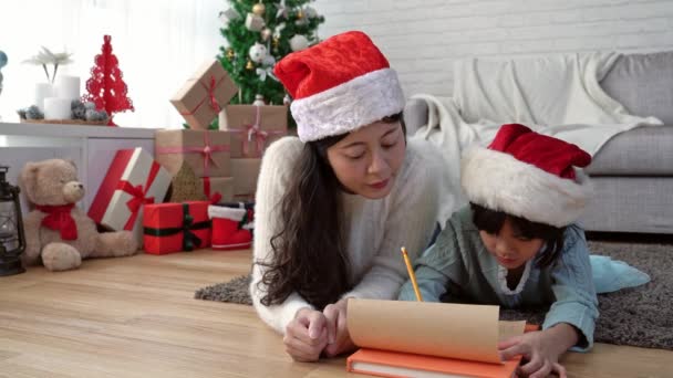 かわいいアジアの子供女の子と彼女の母親 一緒に自宅のリビング ルームの床に横になってサンタ クロースに手紙を書きます クリスマス冬休日コンセプト — ストック動画