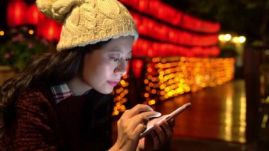 Smartphone manifatura ve aydınlatma ve fener ışık arka plan üzerinde akşam saatlerinde kullanan genç kadın.