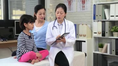 Sevimli küçük kız aile klinikte. Anne kızı destekleyen ve Doktor durumu ve sağlık eğitimi açıklamak için bir dijital tablet kullanarak