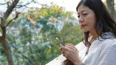 Mutlu Asyalı kız mesaj sms mesajı sonbahar açık havada doğa orman zam üstünde hareket eden telefon. Gülümse ve kamera için yüz