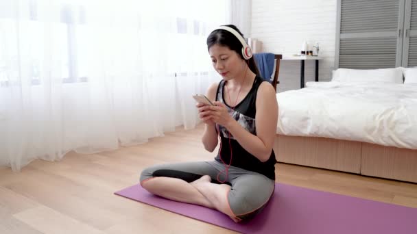 Asiatische Frau Sitzt Auf Der Yogamatte Und Benutzt Ihr Handy — Stockvideo