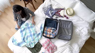 Ona gömlek katlama ve bavulunu ambalaj Asyalı kadın. Yüksek bir açı üzerinde. Bir hızlı hareket.