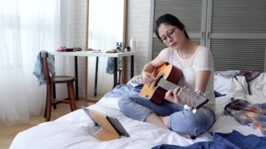 Asyalı kadın onun gitar pitch standartları denetleniyor. O tablet kullanma onun ownself tarafından pratiği yapıyor.