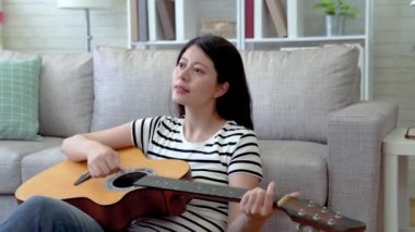 Oturma odasında kanepede oturan ve hoş bir ruh olarak onun gitar oynamaktan Asyalı kadın.