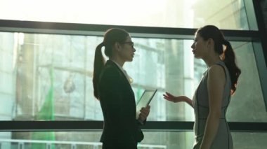Sun işaret fişeği cityscape dışında iki iş kadını pencere yakınındaki siluetleri ve tablo karanlık ofis iç, bir şey tartışmak ve dijital tablet holding.