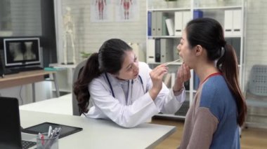 Hastanın boğazını kontrol etmek için tahta bir sopa kullanarak kadın Asyalı doktor.