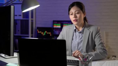 Geç başlatma hisse senedi ofiste çalışan rahat kadın. Yorgun ama mutlu kız kendini sırasında hisse senedi verileri arka planda çalışan dizüstü bilgisayar ile işyerinde germe.