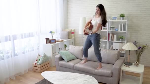 一个亚洲女人站在沙发上弹吉他和跳舞的快速动作 — 图库视频影像
