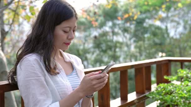 携帯電話の仕事のテキスト メッセージを使用して リゾートで読んでかなりアジアの少女 — ストック動画