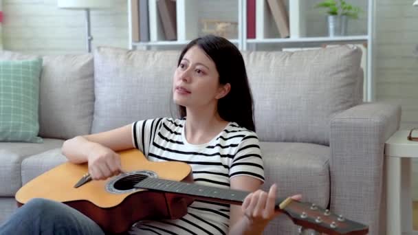 アジアの女性のリビング ルームのソファに座っていると 気持が良い気分での彼女のギターを弾き — ストック動画
