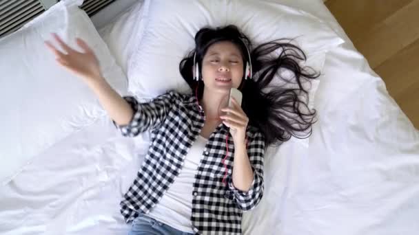亚洲女音乐家听她的最佳的册页并且大声唱歌在床上 — 图库视频影像
