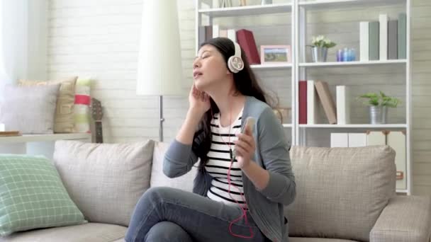 亚洲现代女性在客厅里用耳机里的音乐唱歌 晃动着身体 — 图库视频影像
