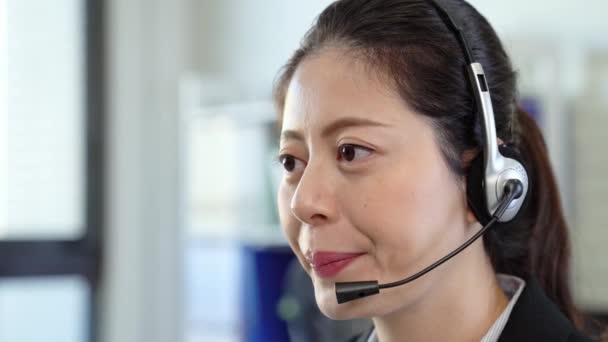 ヘッドセットと問題を解決するために彼女の顧客に役立つ幸せの笑顔で働く若いアジア社員 — ストック動画