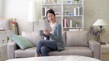 Asyalı kadın onun iş ve sit aşağı kısa bir mola için rahat kanepe bitirdi. O bir yabancı dil gazete okuyor.