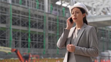 Açık havada ve yapısı bina karşı ayakta iken cep telefonda konuşurken tutan hardhat başarılı kendine güvenen kadın iş mimar.