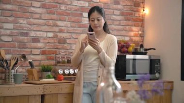 ev kadını mutfakta bir smartphone kullanarak ağır çekim. onun meslektaş için mesaj atıyor. O evde onun işi bitirebilirsiniz. Her nerede ve ne zaman o. internet üzerinden.