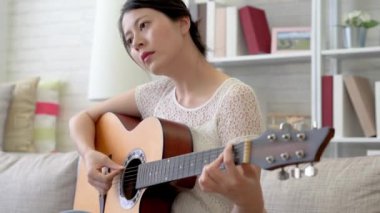 Asyalı kadın gitar çalmak ve parmaklarını iplerde koyarak yakın çekim çekim.