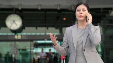 Tren Gar binası dışında gülümseyen smartphone kullanarak profesyonel genç Asya iş kadını.