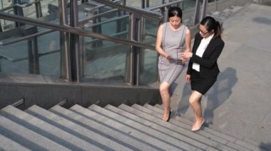 İki Asyalı kadınlar iş ofis binası dışında merdivenlerden yukarı yürürken dijital tablet holding ile söz