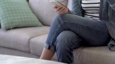 Salonda rahat koltukta oturan ve sıcak içecek ve manifatura onun smartphone tarafından içme Asyalı kadın.