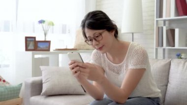 Modern oturma odasında kanepede oturan gözlüklü Asyalı kadın. O apps ve sosyal ağlar üzerinden arkadaşlarıyla sohbet.