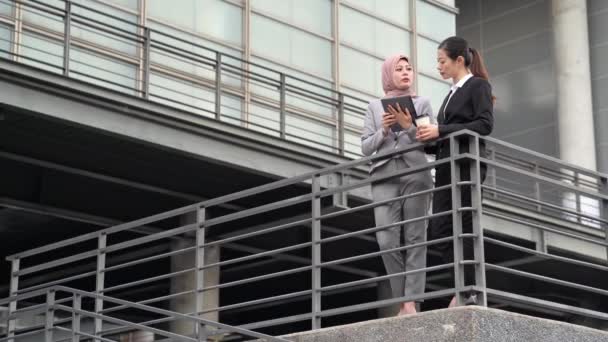 デジタル タブレットを使用して不動産イスラム教徒マネージャー事務所ビルの外に立って彼女のビジネス クライアントに市場を説明します — ストック動画