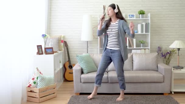 Asian Woman Sings With Her Cellphone As The Microphone And Danced In The Living Room She Follows The Sounds In The Headset And Signs Out The Lyrics Loudly