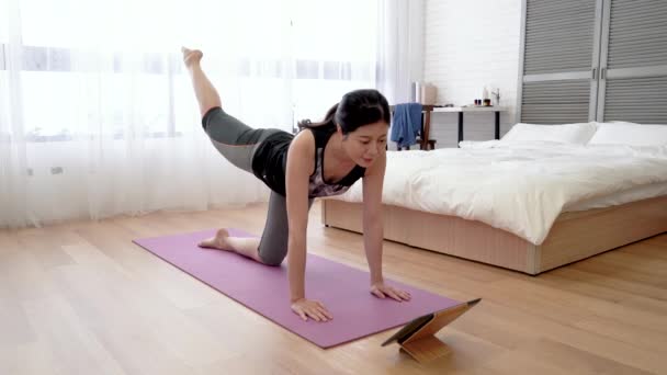 亚洲妇女遵照片剂的指示做练习 她一步步地在瑜伽垫上举起双腿 — 图库视频影像