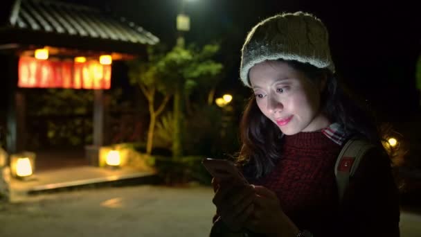 夜立っている入浴の家の門の外で携帯電話のテキスト メッセージを使用して美しい日本の女の子 — ストック動画