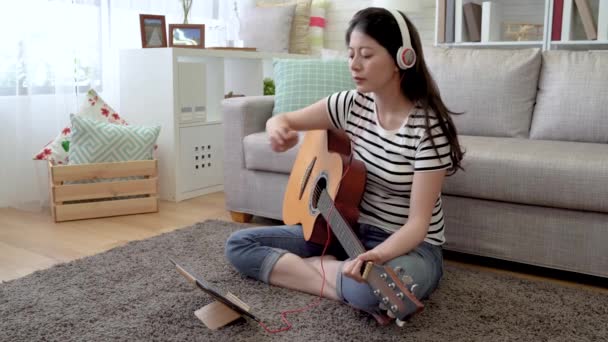 亚洲女吉他手用客厅里的触摸板 用耳机里的音乐哼着歌 数着节拍 — 图库视频影像