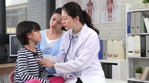 美丽的年轻母亲和她的小女儿在儿科医生 医生正在检查小病人使用听诊器检查肺和心脏和孩子的深呼吸 — 图库视频影像