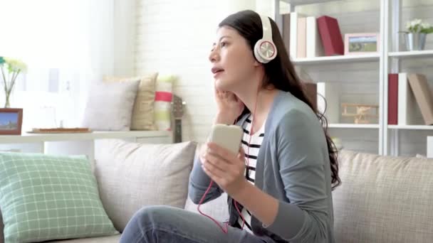 アジアの女性がヘッドフォンを身に着けている彼女のお気に入りの音楽を聴くと曲の後彼女の体が揺れて — ストック動画