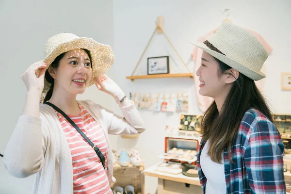 Amigos do sexo feminino compras e tentando chapéus de palha . — Fotografia de Stock