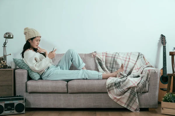 Одинокая грустная девушка смотрит на смартфон на диване — стоковое фото