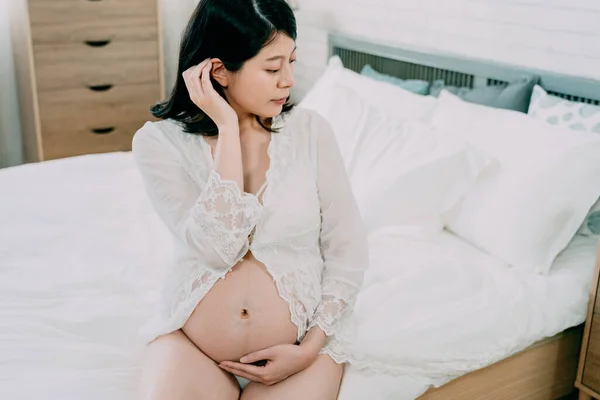 Gorgeous girl on bed hold bare belly expect baby Stock Picture