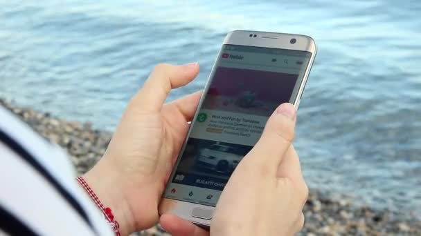 Девушка смотрит YouTube на своем смартфоне на пляже — стоковое видео
