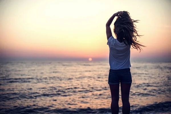 Jovem mulher em pé sobre a pedra, olhando para o pôr do sol sobre o mar — Fotografia de Stock