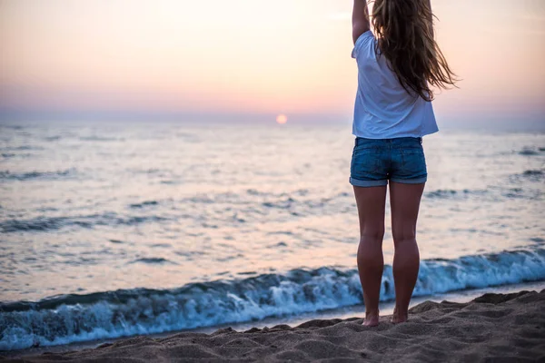 Mujer joven de pie sobre la piedra, mirando el atardecer sobre el mar — Foto de Stock