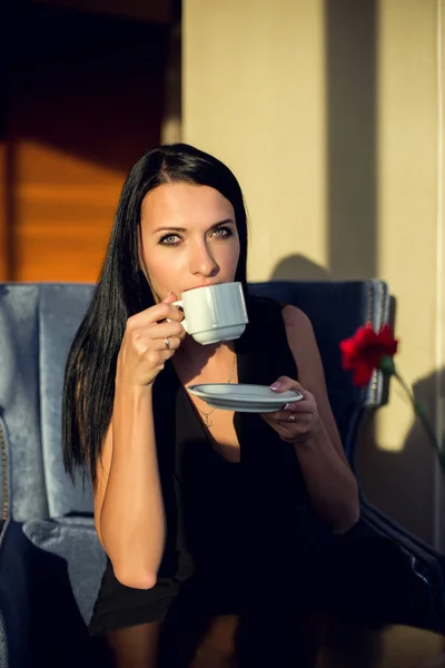 Retrato de una hermosa joven sentada en una mesa con una taza de café — Foto de Stock