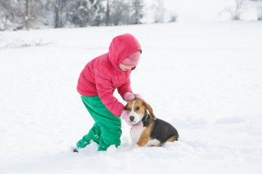 Küçük kız köpeğini karlı bir manzara ile oynarken